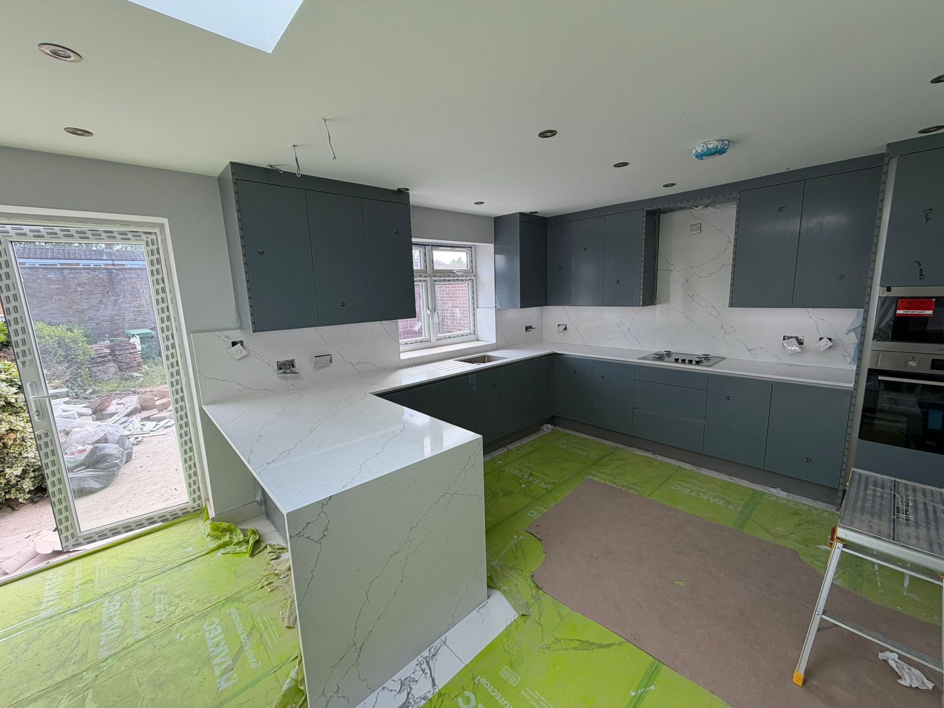 Teal kitchen with white marble worktops and splashback